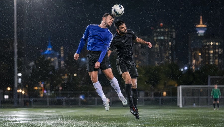 Sample photo: two players rising for a header in the rain under floodlights